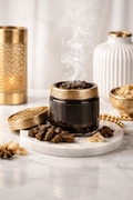 Incense bakhoor product with gold lid on a marble surface with candles. 